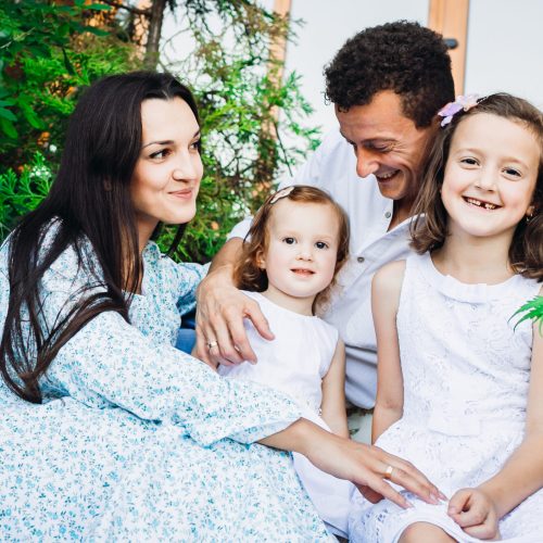 Beautiful brunette woman hugs her little daughters and husband sitting outside