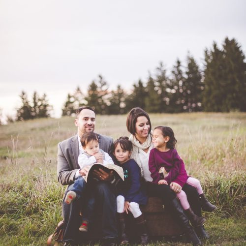 A beautiful cheerful family with a mother, father and three kids reading the Bible in the park